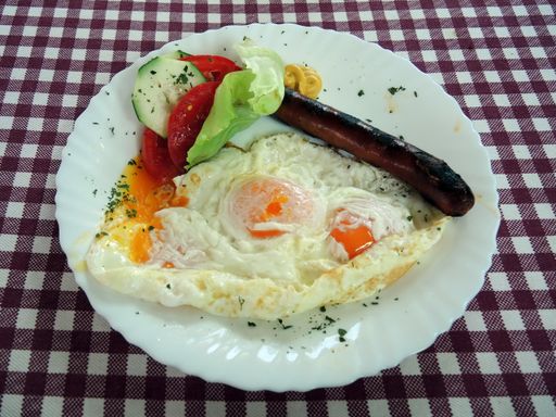 A closeup shot of a delicious breakfast with eggs, sausage and salad on the white plate
