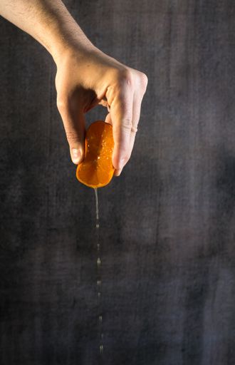 A hand squeezing half of a ripe mandarine in the grunge texture background with a copy space