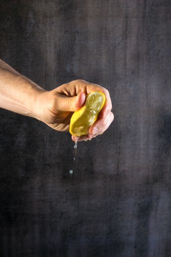 A hand squeezing half of the juicy lemon in the background with a copy space