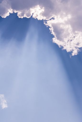 A vertical shot of a beautiful blue sky with sunlight coming through clouds