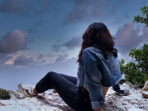 A young woman sitting on a rock, looking up at the sky in twilight