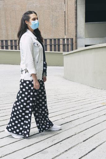 An attractive Hispanic female in a facial mask walking in an outdoor - new normal concept