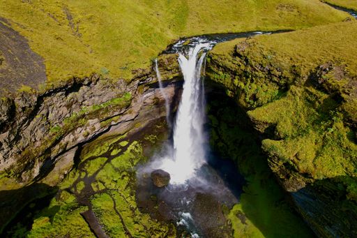 Aerial view of lush landscape featuring waterfall cascading down a rocky cliff face surrounded by lush green trees and vegetation