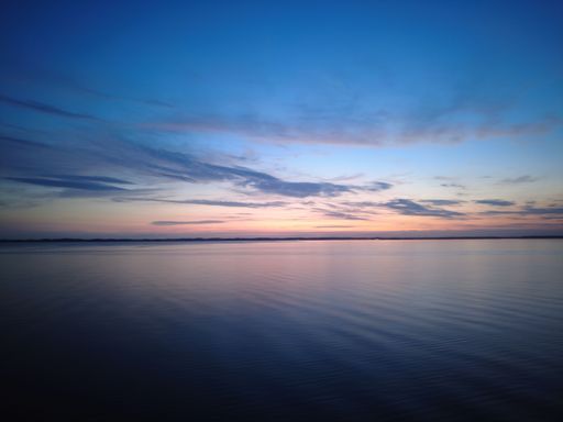 Beautiful sunset on the Sea with blue sky and clouds, colorful sky reflected in the water. Coast of Denmark on the horizon at summer twilight evening