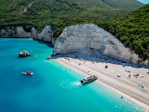 4K Far drone shot of Fteri Beach, Kefalonia, Cephalonia, Greece with the limestone hillside, boat taxis and people sunbathing