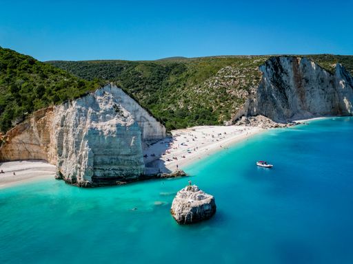 4K Angle shot of Fteri Beach, Kefalonia, Cephalonia, Greece with beach area, rocky hillside, a boat and people swimming in turquoise water