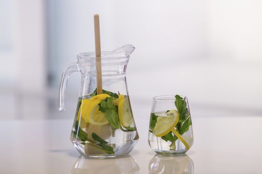 A jar and a glass with lemon slices, mint leaves and a wooden spoon on an out of focus background. Close up. Healthy refreshment concept.