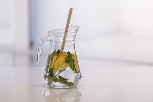Glass jar with freshly cut lemon slices, mint leaves and a wooden spoon on an out of focus background. Close up. Refreshment concept.