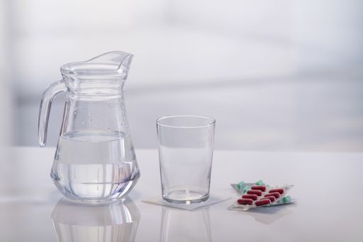 An empty glass surrounded by a jar of water and medicine capsule blisters on an out of focus background. Close up. Medication and healthcare concept.