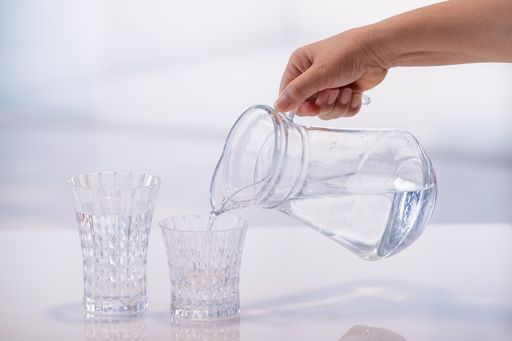 Female hand holding a jar of water and pouring it into a glass on an out of focus background. Selective focus and close up. Water and health concept.