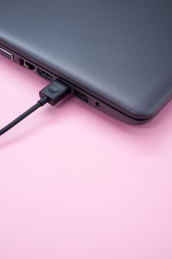 A vertical shot of a black laptop with a cable connected on pastel pink background for a copy space