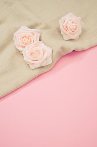 A vertical shot of decorative pink roses on a cream cloth and pink surface for a copy space
