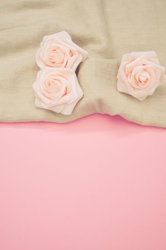 A vertical shot of decorative pink roses on a cream cloth and pink surface for a copy space