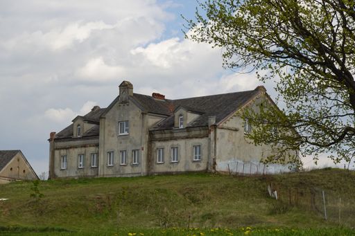 An old, rustic, country house sits atop a hill, with vibrant flowers in full bloom in the surrounding lawn