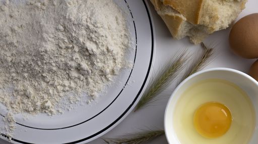 An overhead shot of flour in a plate and eggs next to it on a white a table