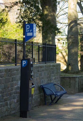 A vertical shot of a bench near a parking payment terminal
