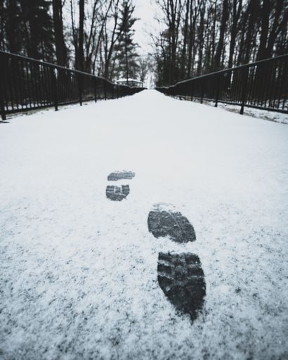 A vertical shot of footsteps on the snow on a path surrounded b