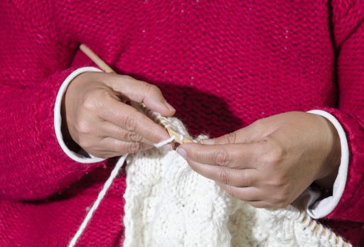 A female in a pink sweater knitting a white clothing