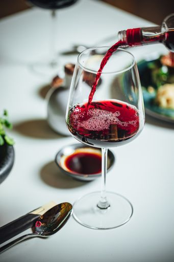 A selective focus shot of pouring red wine into the glass on a white table