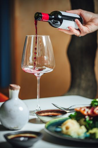 A selective focus shot of pouring red wine into the glass on a white table