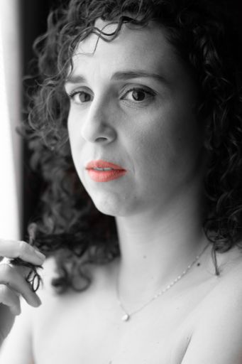 A vertical grayscale shot of a female with curly hair and red li