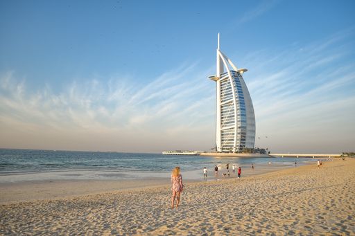 A back view of a young blonde female on Jumeirah Beach and luxury Burj al Arab hotel in background, Dubai, United Arab Emirates