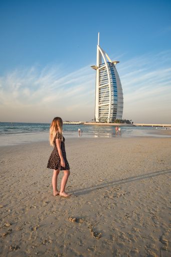 A back view of a young blonde female on Jumeirah Beach and luxury Burj al Arab hotel in background, Dubai, United Arab Emirates
