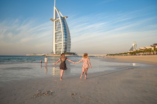 A back view of a young blonde female on Jumeirah Beach and luxury Burj al Arab hotel in background, Dubai, United Arab Emirates