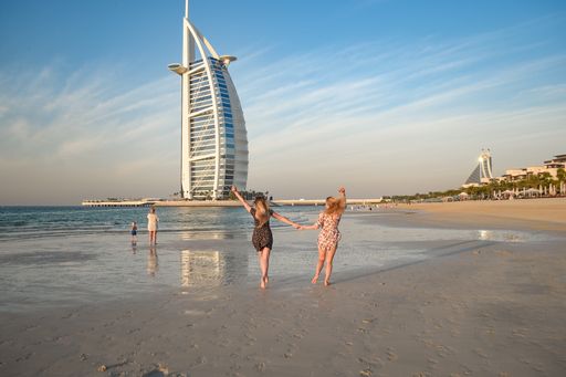 A back view of a young blonde female on Jumeirah Beach and luxury Burj al Arab hotel in background, Dubai, United Arab Emirates