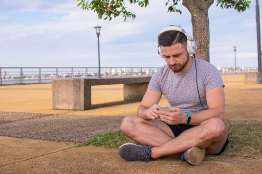 A closeup shot of a male wearing headphones and looking at his phone while sitting in the park
