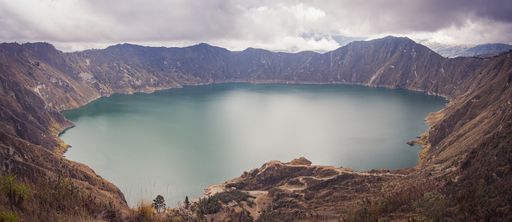 A panoramic shot of the Quilotoa Lake surrounded by hills under a cloudy sky in Ecuador