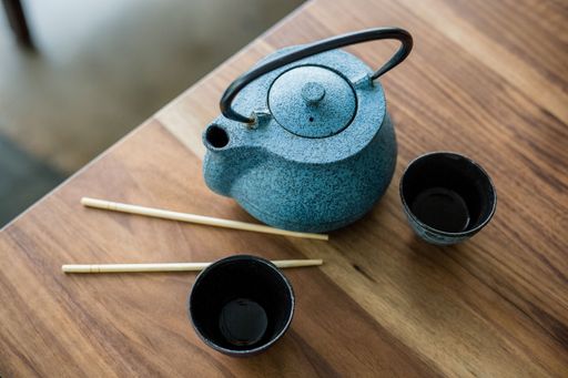 A closeup shot of a blue teapot, small glasses of tea, and chopsticks on a brown surface