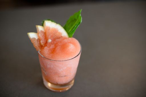 A small glass of iced pink cocktail with grapefruit slices on a table