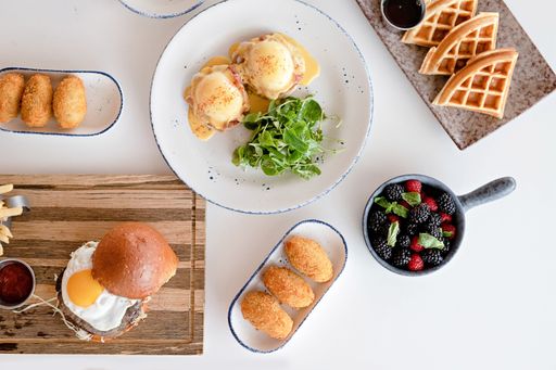A top view of a table with gourmet breakfast dishes like waffles, egg benedict, and berries