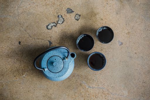 A top view of a blue teapot and small glasses of tea on a brown surface
