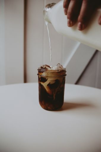 A female's hand pouring cream into a cup of Glasse on a white table