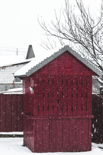 A vertical shot of a red small barn covered with snow