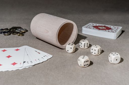 A closeup of playing cards with dice and a wooden cup on the table with coins on it