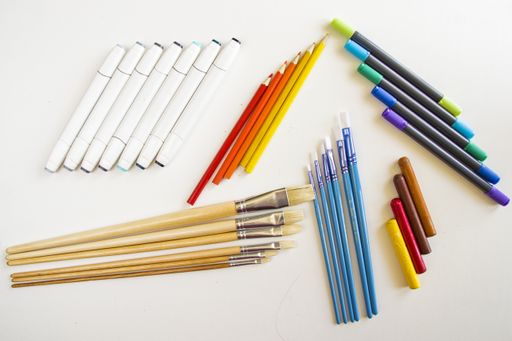 A top view of paintbrushes and crayons with colorful markers and pencils on a white surface