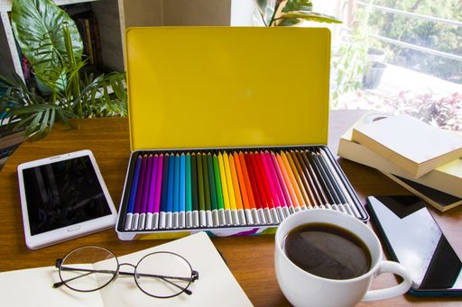 An artist's workplace desk with professional drawing supplies, circular glasses, a cup of coffee, and a tablet