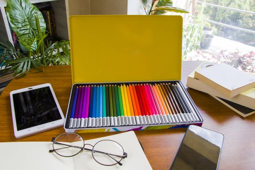 A desk with sketching pencils and sketchbook, empty paper and colorful pencils