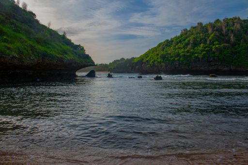 Lagoon bay surrounded from green rock hills. View on the smooth sea waves and cloud sky. Empty fresh water ready for swimm at Kasap beach on Java.