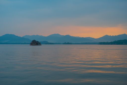 A beautiful view of a lake with rocks in it and mountains on the background during the sunset