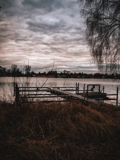 A vertical shot of a dock near a lake on a gloomy day