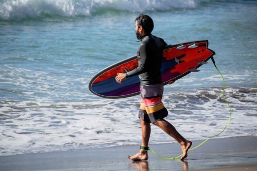 View of surfer with colorful surfboard entering water at Piha beach, Auckland, New Zealand