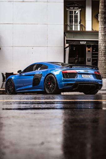 A blue four-door audi car parked in front of a modern high-rise building