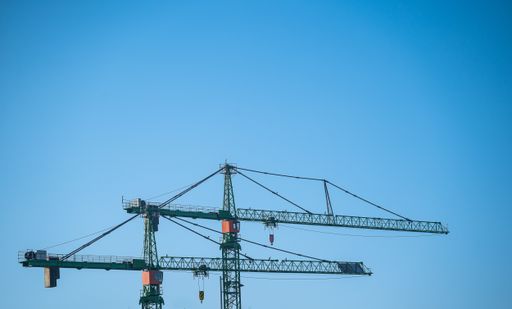 A low angle shot of two idle construction cranes under clear blue sky