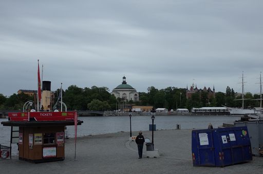 A man standing by an empty ferry ticket booth watching a woman walk away from him in Stockholm, Sweden.