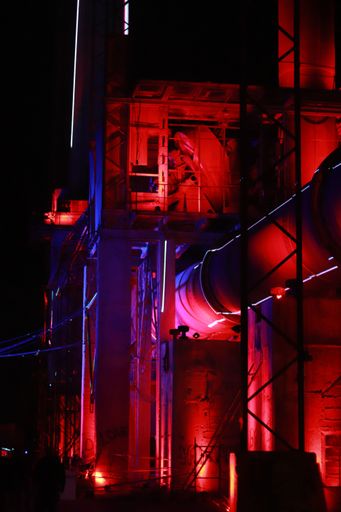 A vertical shot of an industrial building at night illuminated with neon blue and red lights
