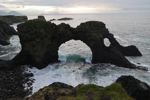 A scenic view of an ancient stone archway situated on the edge of the sea in Arnarstapi, Iceland.